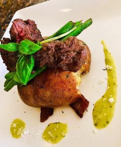 seared steak on top of a deep fried potato, with greens beans and bacon